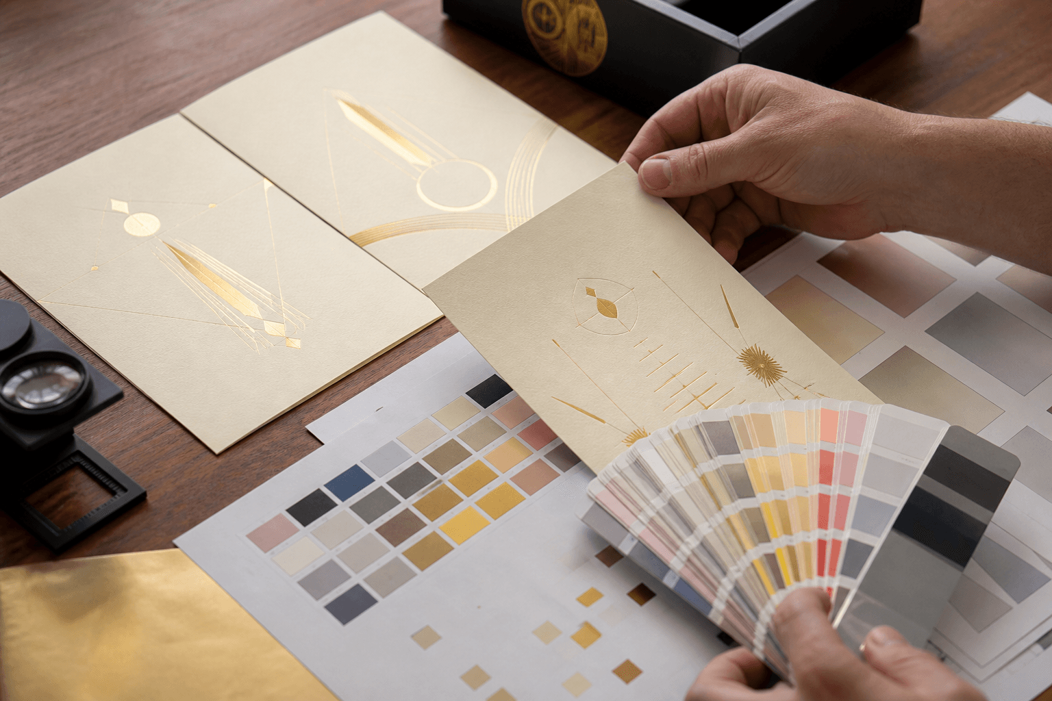Colour proofs and gold-foil visiting cards being reviewed at the design desk